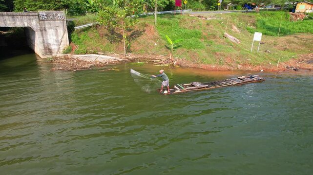 Aerial drone footage of a fisherman nearby the border of the lake, in process of throwing a fishing net from a wooden embarkation, in Jatigede reservoir, Sumedang regency, Java island, Indonesia 