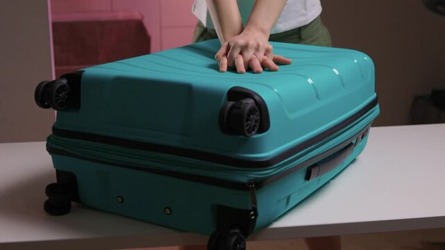 Traveler opening luggage, Close shot of hands unfastening suitcase zipper before travel, Detailed view of hands pulling zipper on vibrant teal travel case with anticipation