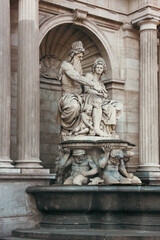 Obraz premium Detailed view of an ornate Baroque fountain sculpture in Vienna, Austria, featuring classical mythological figures carved in stone against a grand architectural facade with columns and arches. 