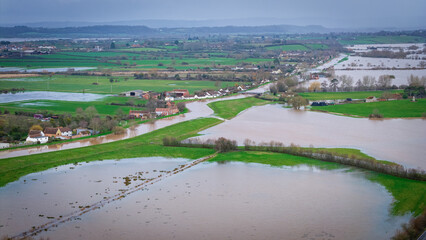 Aerial and ground-level views showing extensive flooding across the Somerset Levels near Burrowbridge, Somerset, following prolonged heavy rainfall. Farmland, roads, rivers, and industrial areas are s