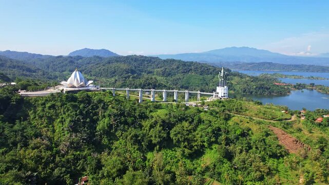 Aerial drone footage of the bridge between the lotus flower shape Al Kamil mosque and Kujang tower, with mountains behind, forests around,in Jatigede reservoir, Sumedang regency, Java island,Indonesia