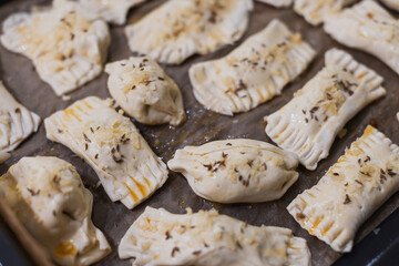 Raw pastry parcels topped with spices and cheese on a baking sheet.