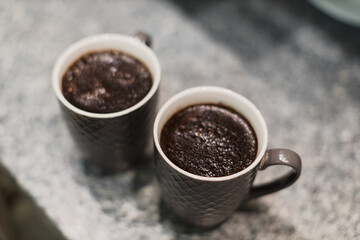 Obraz premium Two chocolate mug cakes sit side-by-side on a speckled countertop.