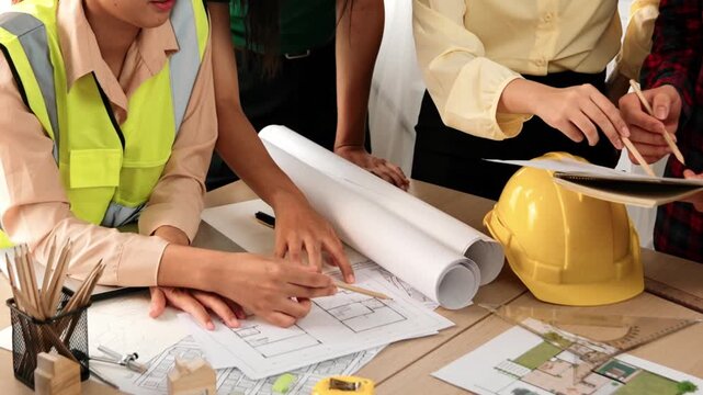 Smart architect and safety engineer discussion about building blueprint on table with architectural document, measurement tools and wooden block scatter around at modern office. Closeup. Delineation.