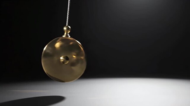 Brass pendulum swings with spotlight illumination and shadow