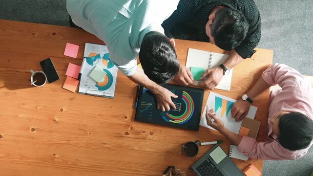 Top view of skilled project manager talking about financial graph to investors while sitting at meeting table with data analysis document. Diverse team discussing and brainstorming idea. Convocation.