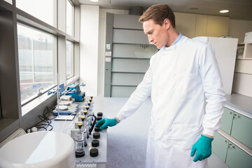 Male tech in lab coat, gloves adjusting pump knobs monitoring vessels tubing at bench, copy space