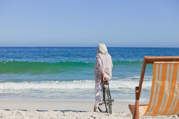 Bicycle is leaning in wet sand near striped orange-and-white chair while waves are lapping