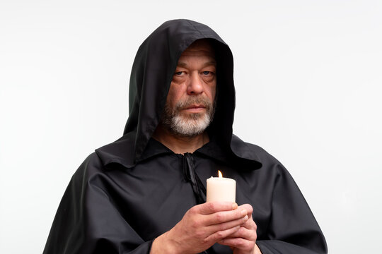 Elderly bearded monk holding lit candle isolated on white background.