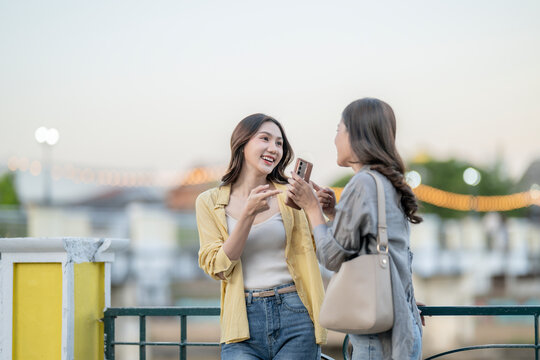 Two asian women laughing sharing smartphone content outdoors