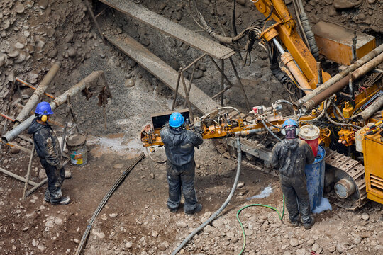 construction workers in protective gear operating a large yellow hydraulic drilling rig inside a deep excavation pit on an urban construction site. Drilling Team Working on High-Rise Building 