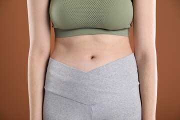 Woman in sportswear after weight loss on brown background, closeup