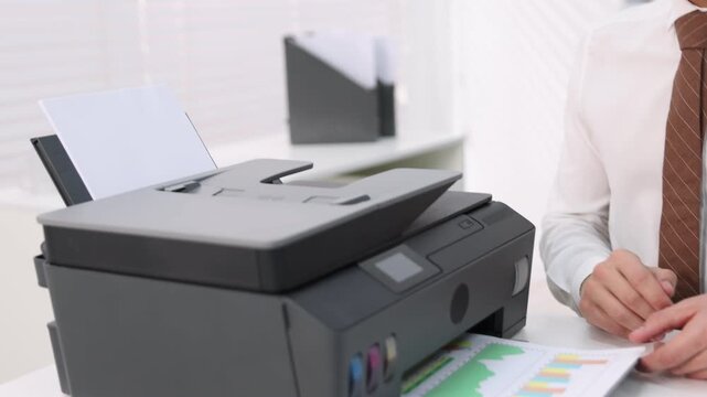 Man working with printer at white desk in office, closeup. Camera moving right and down