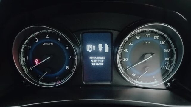 Illuminated car instrument cluster showing analog tachometer and speedometer with white markings, digital display clock and date, fuel and temperature gauges on dashboard.
