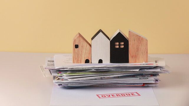 Overdue mortgage concept with stack of bills and wooden house models illustrating debt and financial stress over late payments