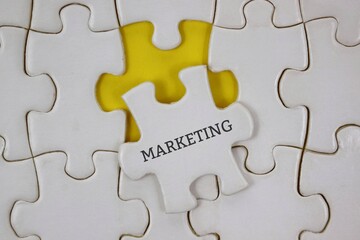 Fototapeta premium white puzzle piece labeled MARKETING sits among others on a yellow background, symbolizing strategic thinking and collaboration.