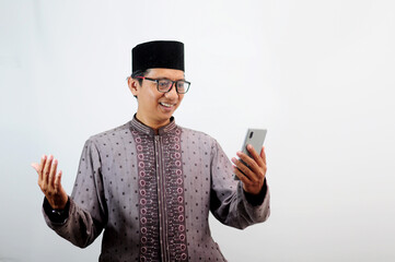 An Asian Muslim man smiles happily while sending a message using his mobile phone, isolated on white background