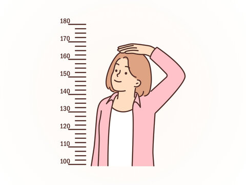 Smiling Young Woman Measuring her Height Against the Wall Scale