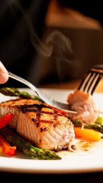 Steaming grilled salmon fillet being cut on a plate with vegetables. Hands, fork, knife