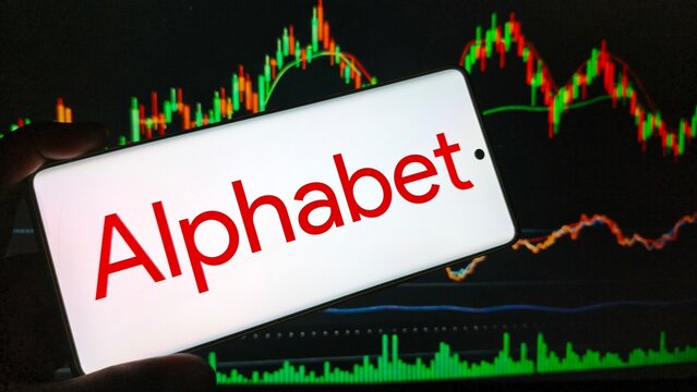 Hand holding smartphone with Alphabet logo on screen in front of stock market graph