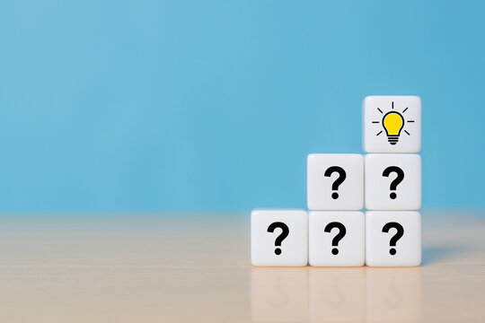 Pyramid of dice or cubes with question mark symbol icons stacked on wooden table with light bulb symbol on top, faq, question and answer or support concept