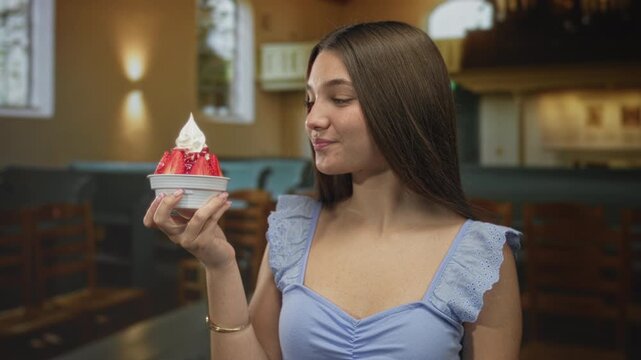 Girl in blue dress holds strawberry bowl and points finger to dessert in historic church hall; delight.