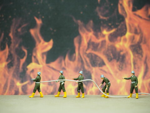 Miniature toy of people at table with blurred fire as a background. Firefighter Crew concept design.