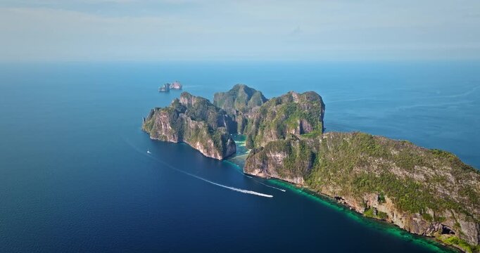 Tropical Phi Phi island displaying lush green limestone cliffs rising from turquoise water with boat cruising past, offering a stunning travel destination and vacation landscape. Aerial drone panorama