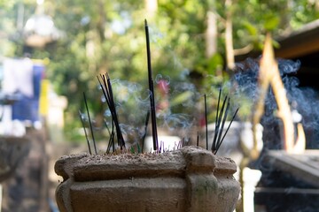Incense sticks emitting fragrant smoke in a serene outdoor setting.