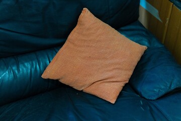 An orange pillow rests on a dark leather couch, creating a cozy and inviting contrast.