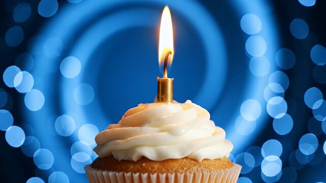 Golden Candle Flame on Creamy White Icing Topped Cupcake with Blurry Blue Bokeh Lights Background