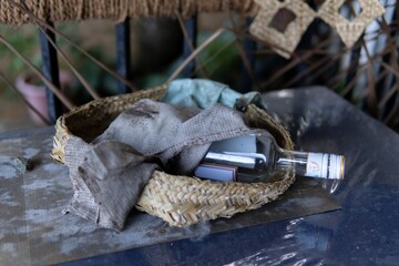 A woven basket holds an empty glass bottle and cloths on a reflective surface.