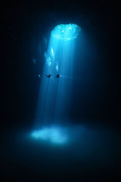 Underwater cave diver silhouettes with light beams in cenote