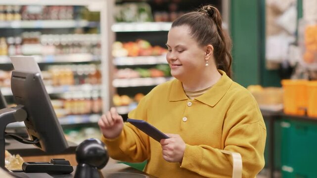 Young Caucasian woman with Down syndrome using self-service checkout and smartphone to buy goods in modern supermarket