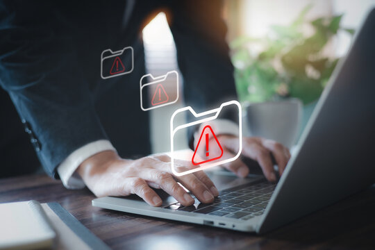 Business person typing on laptop with red warning folder icons. Concept of data breach, corrupted file error, ransomware cyber attack, malware virus, and hacked document information security.