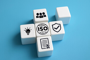 ISO certification concept with teamwork, innovation, documentation, and quality assurance icons on white cubes. Business standards, compliance, and organizational excellence on blue background.