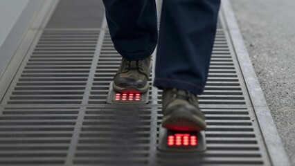 Person walking on metal grate with illuminated red lights underfoot feet