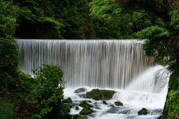 This photograph captures the unique circular waterfall within Guizhou's Xiaoqikong scenic area, where water cascades smoothly over a rounded limestone formation into a clear turquoise pool below. © TAO