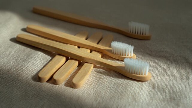 Minimalist Bamboo Toothbrush Set on Linen. Sustainable Packaging & Eco-Friendly Product Shoots. three bamboo toothbrushes arranged linearly and parallel on a textured natural unbleached linen fabric.
