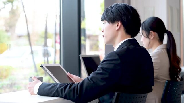 オシャレなカフェやオフィス空間で、タブレットを使う若い男性　転職で悩んだり考えるノマドワーカーなどのイメージ