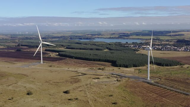 Drone shot of two wind turbines in Airdrie, Scotland near a pine forest.