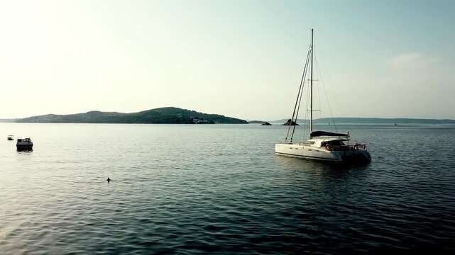 Aerial dolly of single catamaran sailboat anchored on open water near distant islands, Seget Vranjica Croatia