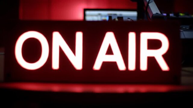 Modern minimalist 'ON AIR' sign with vibrant red glow, slow push-in over blurred high-tech studio equipment in background, rich crimson ambiance, creating a cutting-edge high-fidelity broadcast