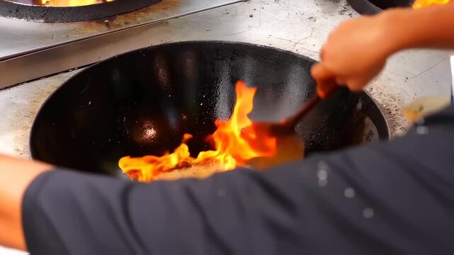 A wok with a fiery flame being stoked with a spatula