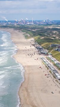 row white beach huts along sandy shore hilltop road behind industrial complex visible distant horizon zandvoort coastline high angle aerial drone view netherlands dutch coast 