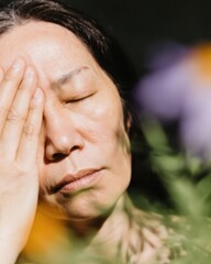 Fototapeta premium Mature Woman Practicing Mindfulness with Closed Eyes and Hand on Face for Pressure Relief in a Lush Garden Setting for Health and Wellness Magazine Content