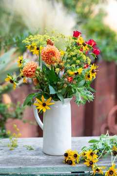 A pitcher of garden flowers outdoors on a potting bench