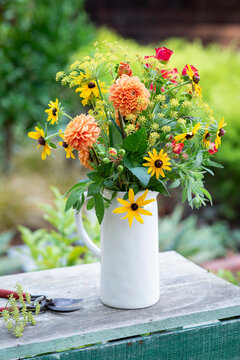 A pitcher of garden flowers outdoors on a potting bench