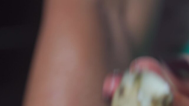 A person carefully peels the shell off a small, boiled speckled quail egg. High detail focus on hands and texture of the eggshell.