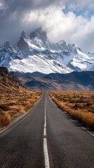 Fototapeta premium Vibrant photo of Long straight road leading to majestic snow capped mountains under a dramatic sky